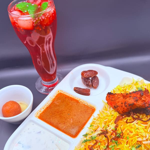 Indian biryani meal with chicken, rice, sauces, dates, gulab jamun, and a red drink.