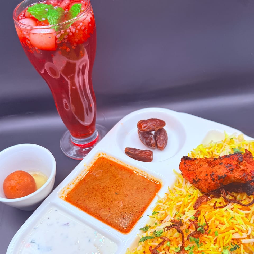 Indian biryani meal with chicken, rice, sauces, dates, gulab jamun, and a red drink.
