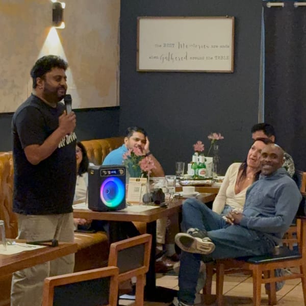A man speaks into a microphone at House of Biryanis and Kebabs, while guests listen at tables.